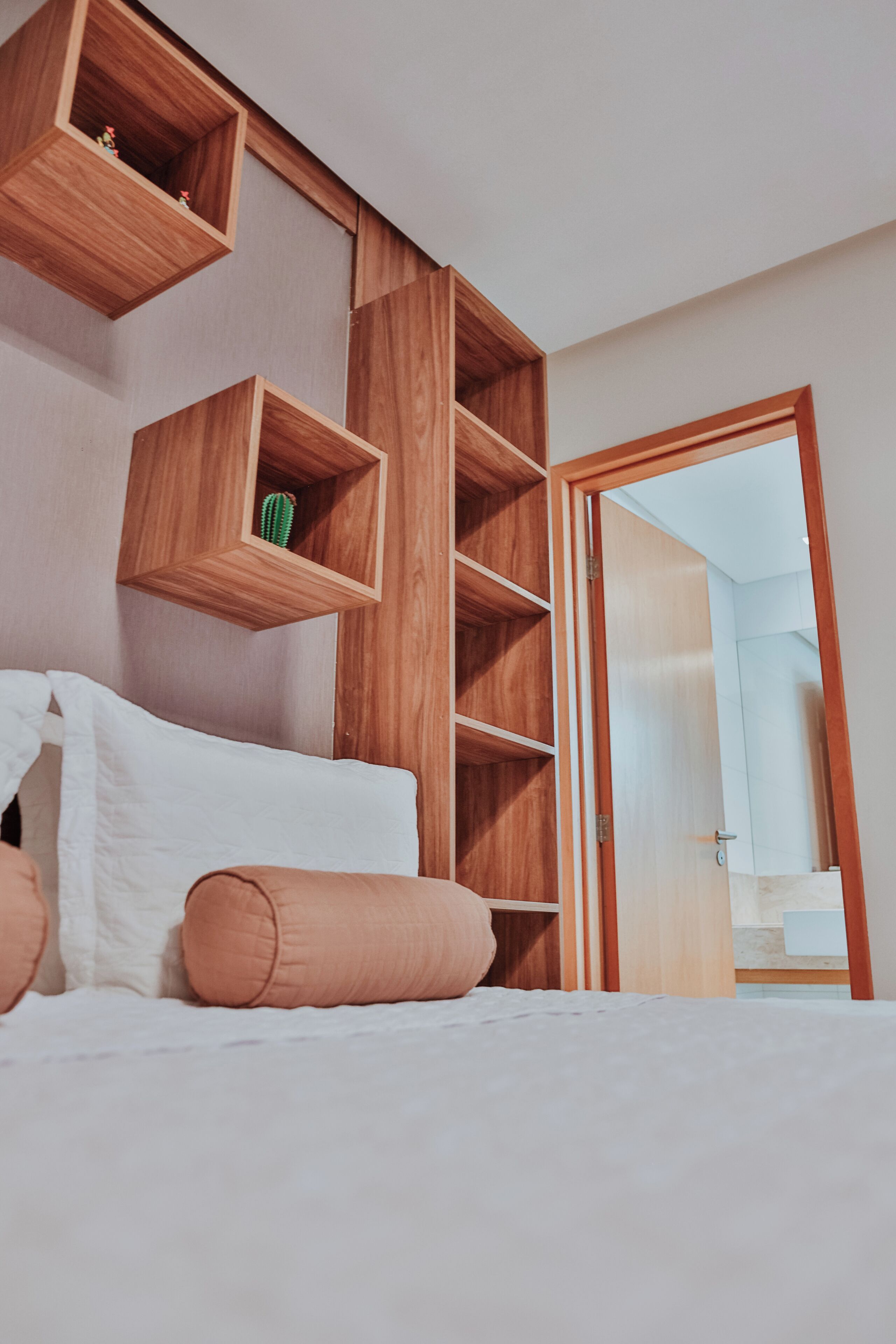 Une chambre à coucher comprenant un lit, une étagère en bois et une porte donnant accès à une salle de bain.