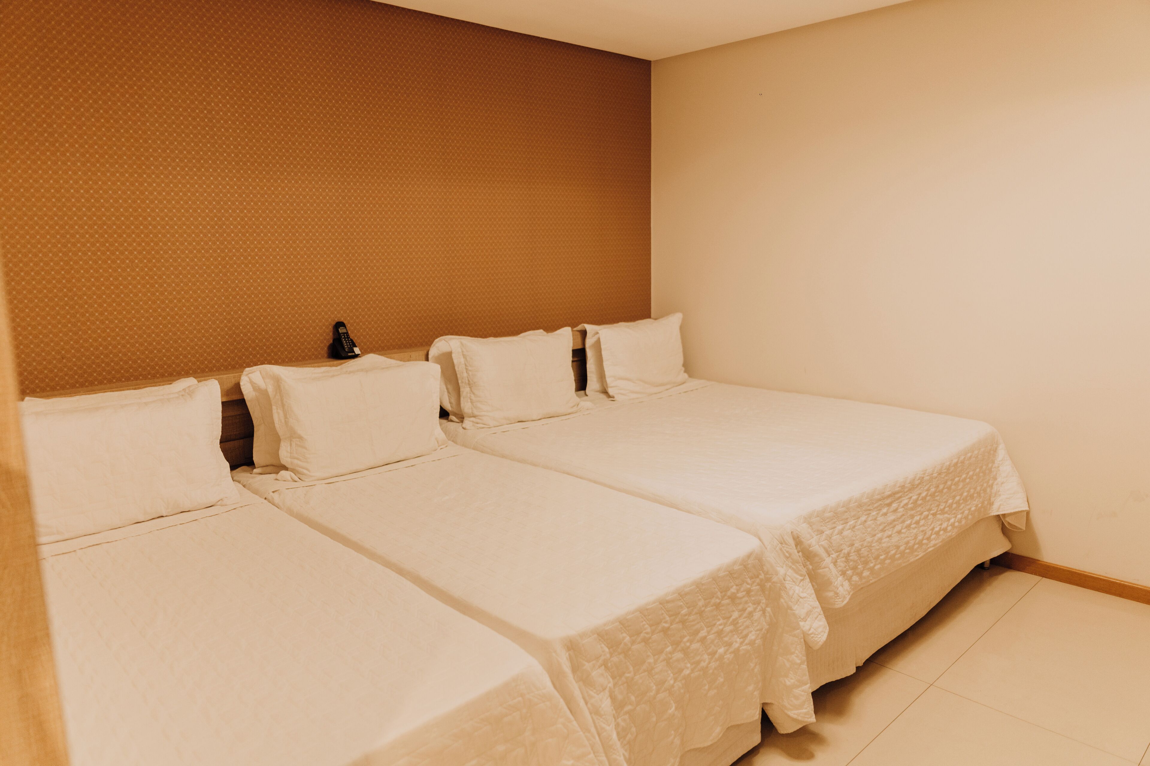 Une chambre d’hôtel avec deux lits simples, une tête de lit en bois et un mur sobre.