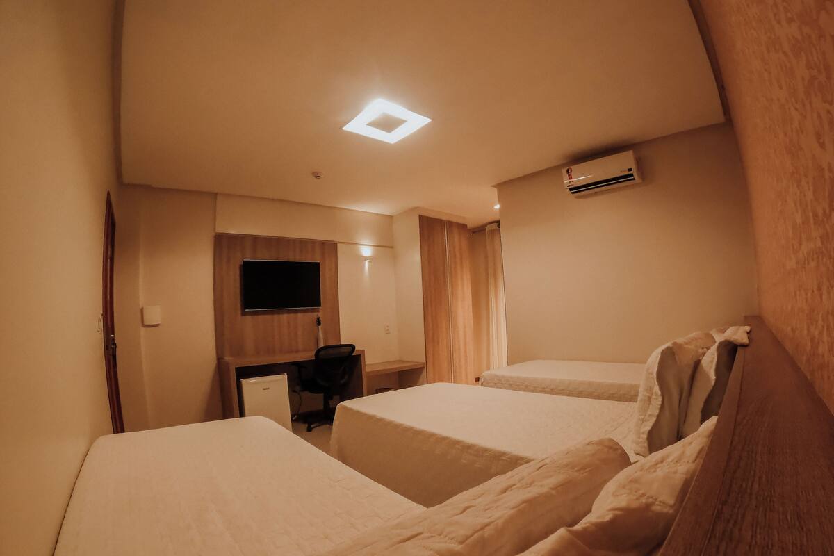 Quarto de hotel com duas camas, uma escrivaninha, uma televisão e um ar condicionado.