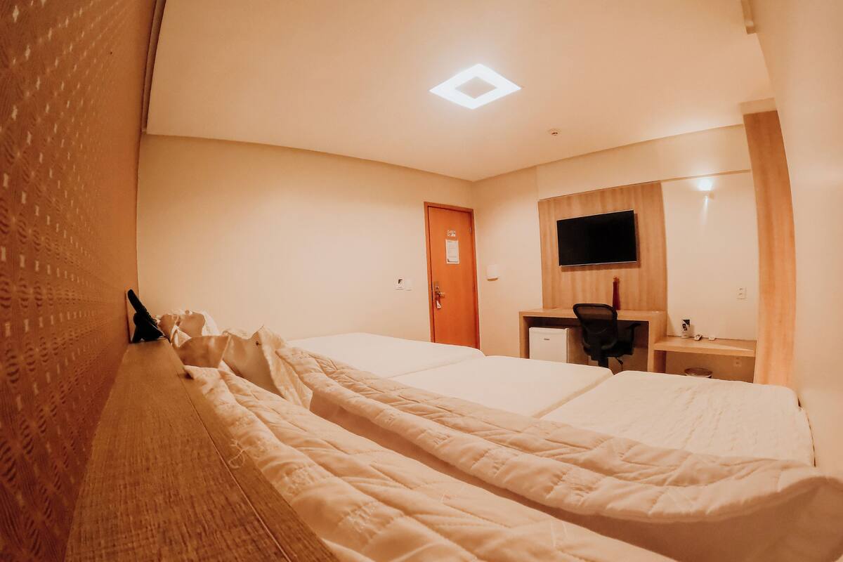 Quarto de hotel com duas camas, uma escrivaninha, uma cadeira, uma televisão e uma porta.