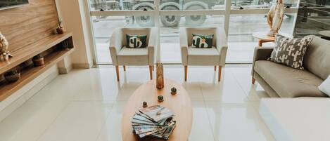 A modern hotel lobby with a wooden coffee table, two armchairs, a sofa, and a TV on a wooden shelf.