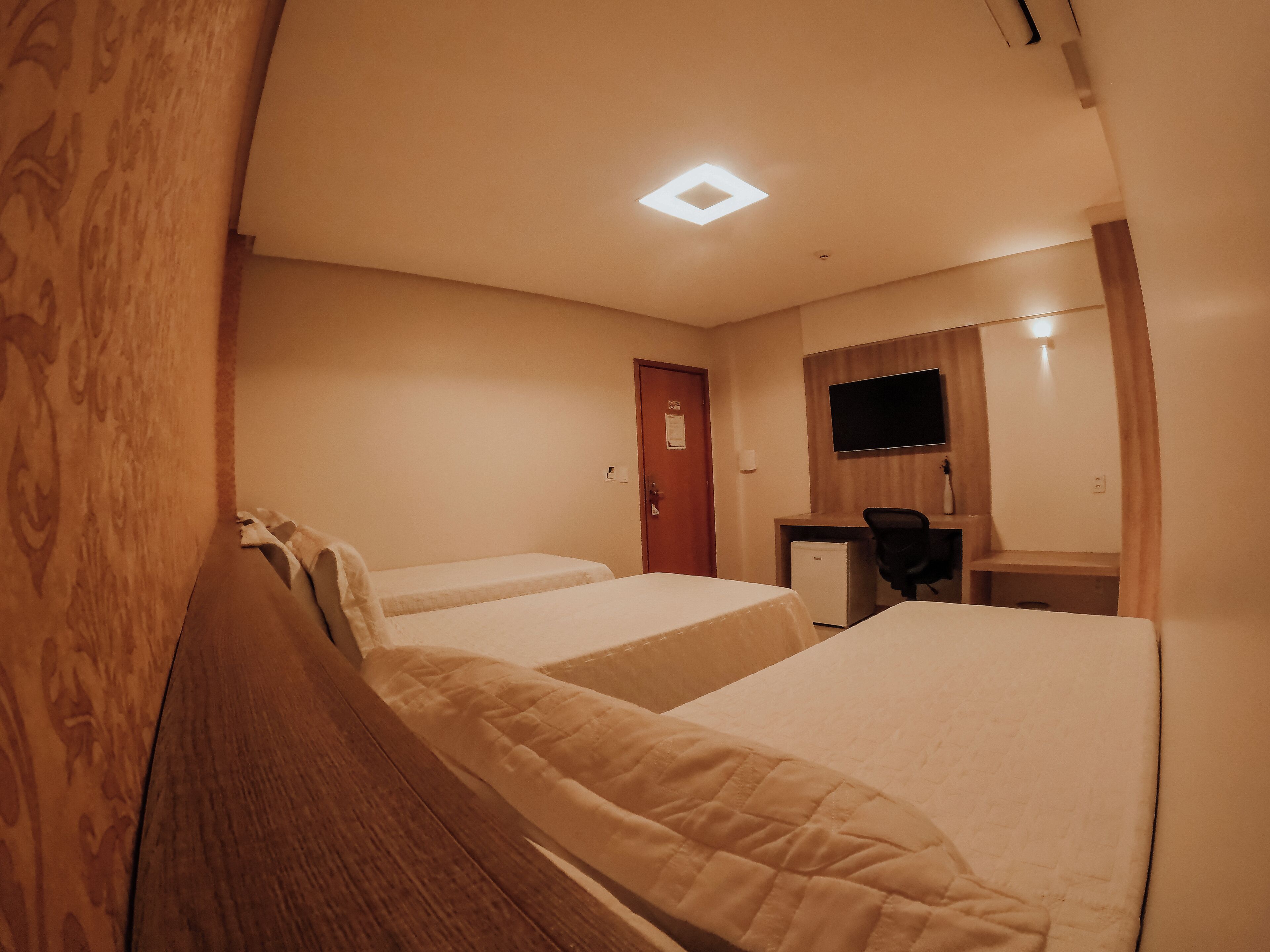 Een hotelkamer met twee bedden, een bureau, een stoel, een televisie en een kleine koelkast.