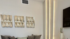 A modern living room with a grey sofa, decorative wall art, a round coffee table, and a patterned rug. - 4731-103 Stay Magical • 2BR with Mickey Room & More (Kissimmee)