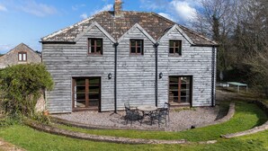 Una casa in legno con tetto in tegole, un camino e un piccolo patio con tavolo e sedie.