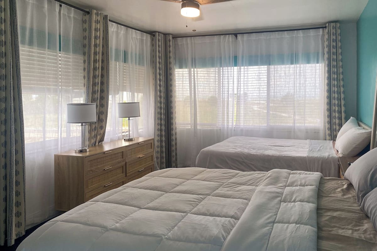 A hotel room with two beds, a wooden dresser, and a ceiling fan.