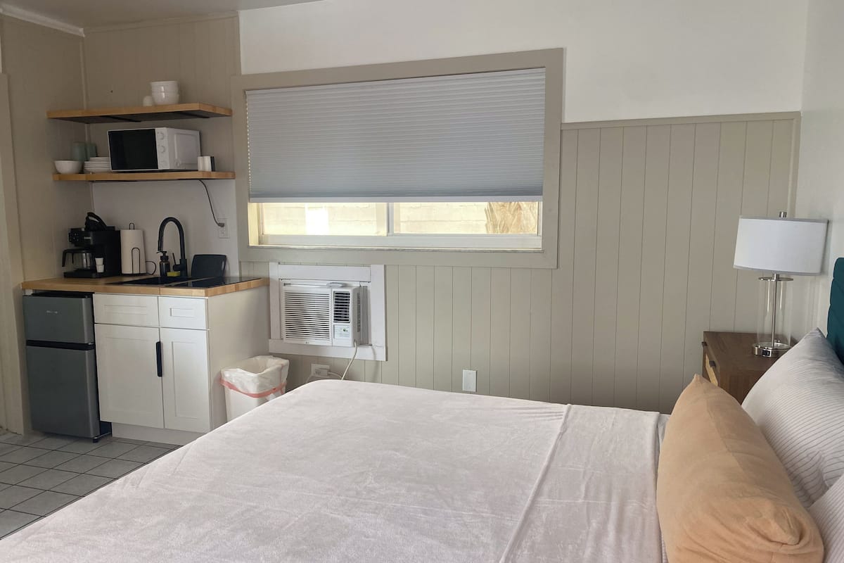 A hotel room with a bed, a desk with a microwave, a coffee maker, and a window with blinds.