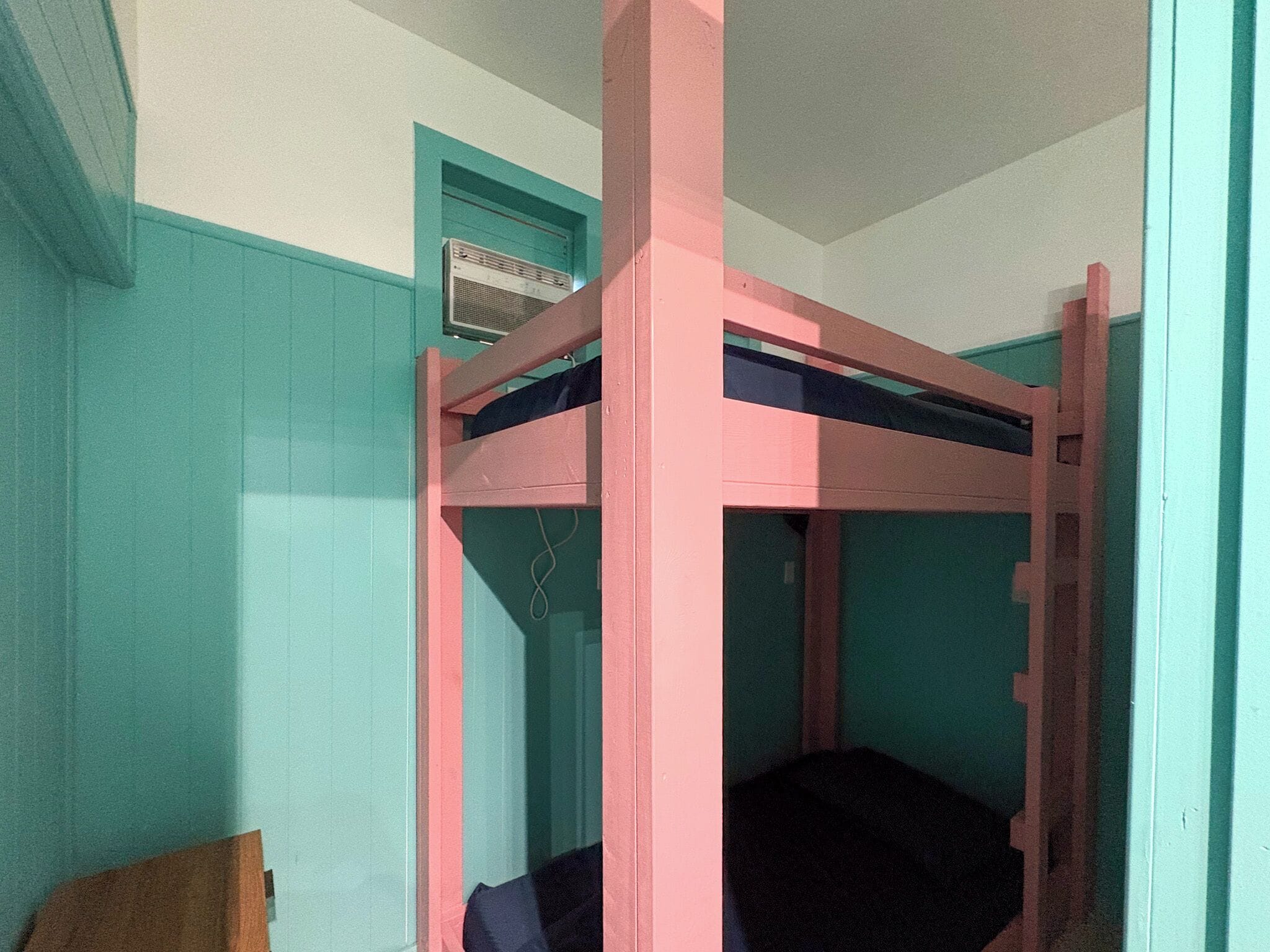 A bunk bed with a pink frame and a single bed below.