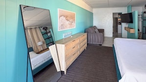 Een kamer met turquoise muren, een bed, een dressoir, een spiegel, een ingelijst kunstwerk en een televisie.