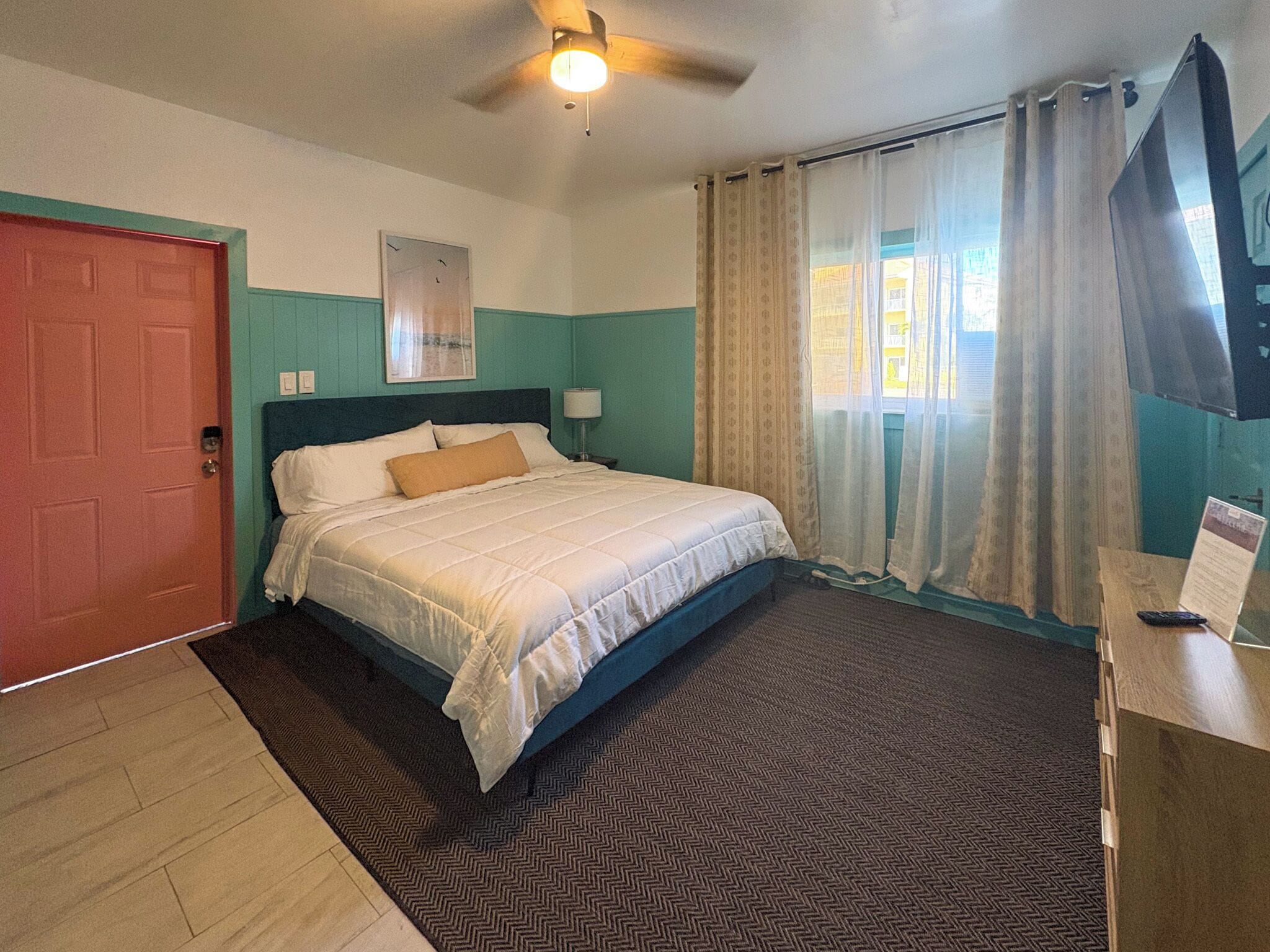 Un dormitorio con cama, ventilador de techo, puerta y ventana con cortinas.