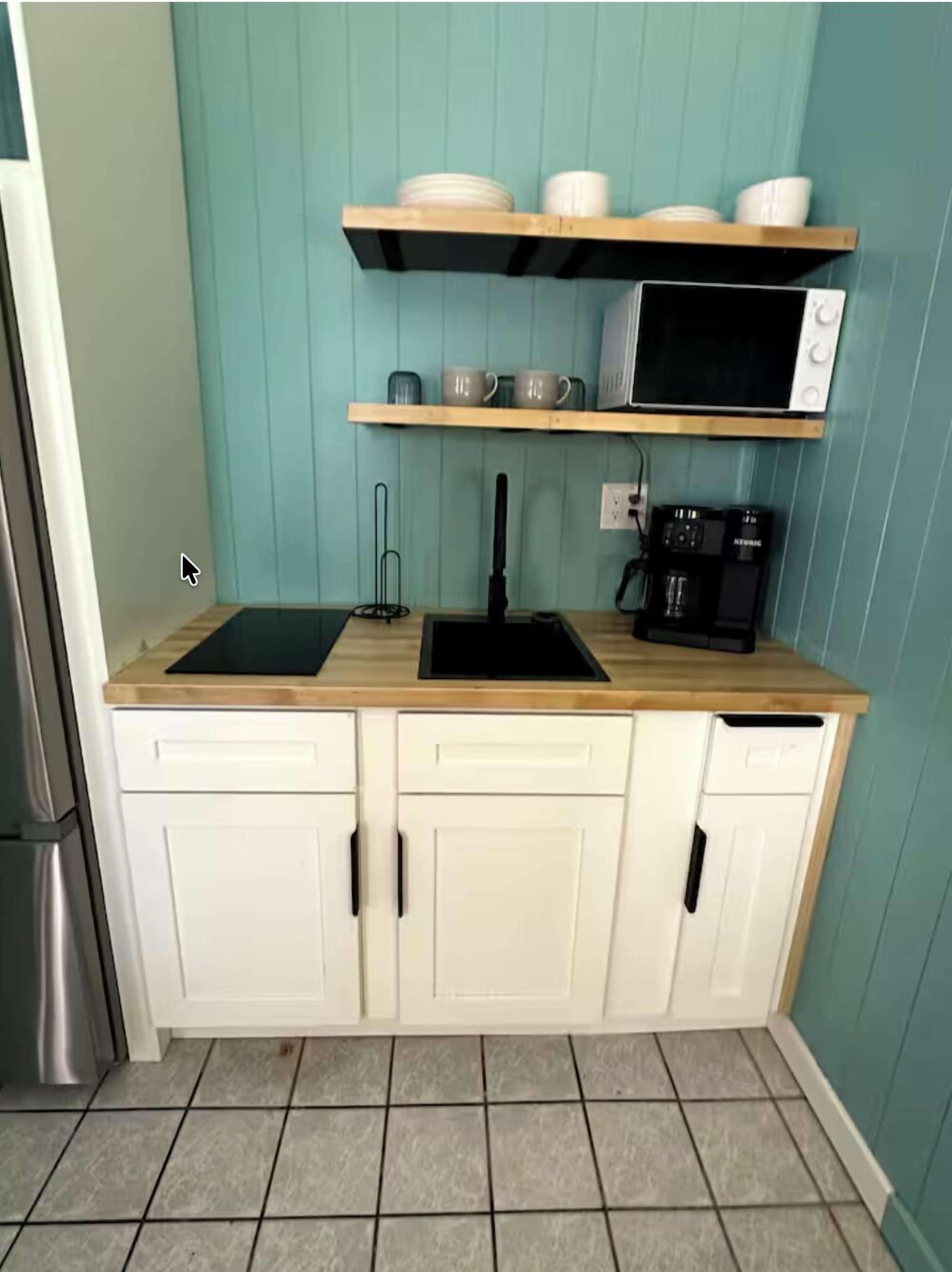Una cocina con encimera de madera, armarios blancos, microondas, cafetera y lavabo.