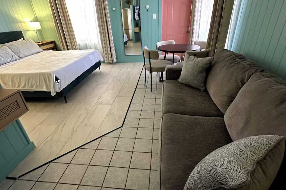 A room with a bed, a sofa, a dining table, and a mirror.