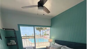 Een slaapkamer met een bed, een plafondventilator, een raam met uitzicht op een zwembad en een balkon.