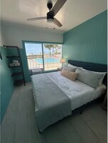 A bedroom with a bed, a ceiling fan, a window with a view of a pool, and a balcony.