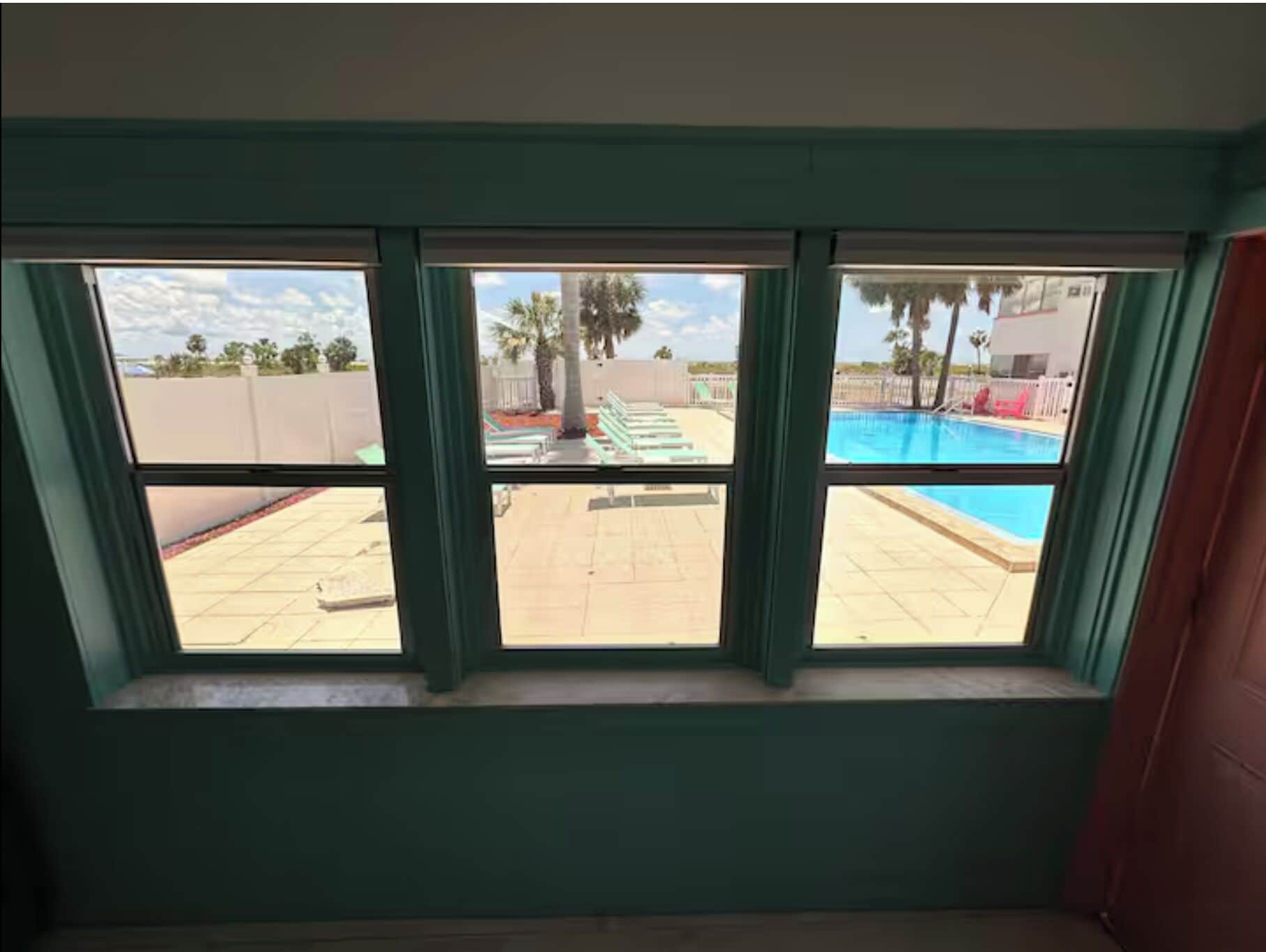 A room with a view of a swimming pool, a patio area, and a fenced outdoor space.