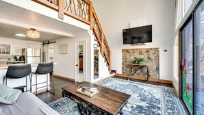 Un vaste espace de vie agrémenté d’un escalier en bois, une cuisine à l’arrière-plan et une grande fenêtre.