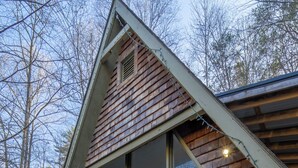 Une cabane dotée d’un toit en pente, de grandes fenêtres et de fondations en pierre.