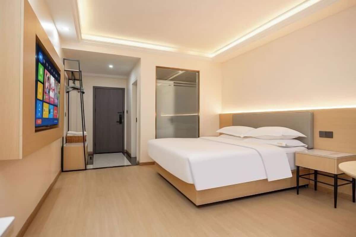 A modern hotel room with a large bed, bedside table, and a mirror. There is a wardrobe with a mirror and a door leading to another room.