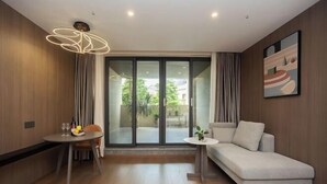 Una sala moderna con un sofá, una mesa de comedor con sillas, una mesita auxiliar y un amplio ventanal corredero que da a un espacio al aire libre.