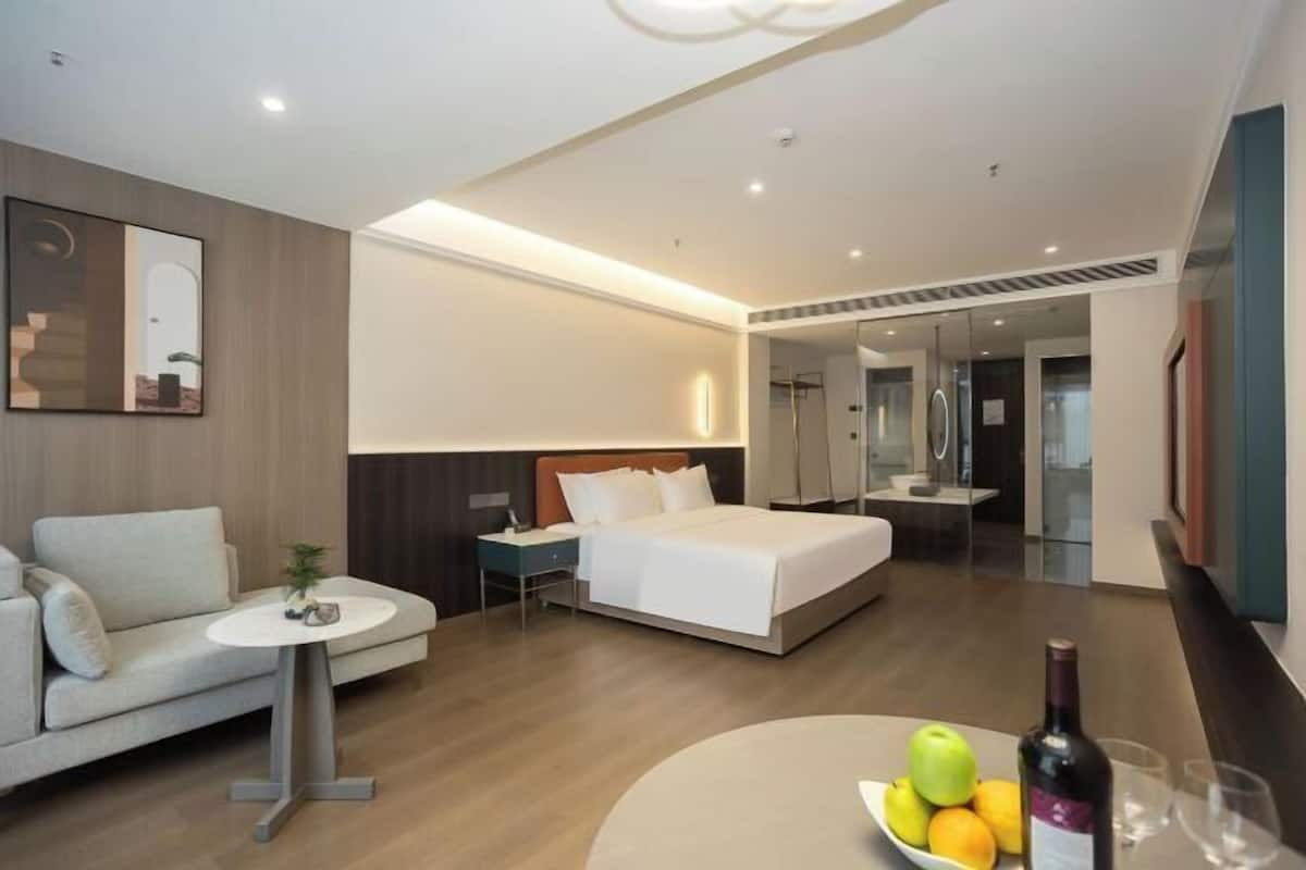 A modern hotel room with a bed, a sofa, a small table, and a fruit bowl.