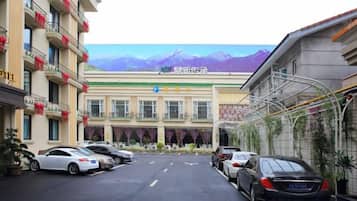 Un hotel con estacionamiento, un edificio con cartel y montañas al fondo.
