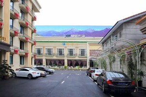 Un hotel con estacionamiento, un edificio con cartel y montañas al fondo.