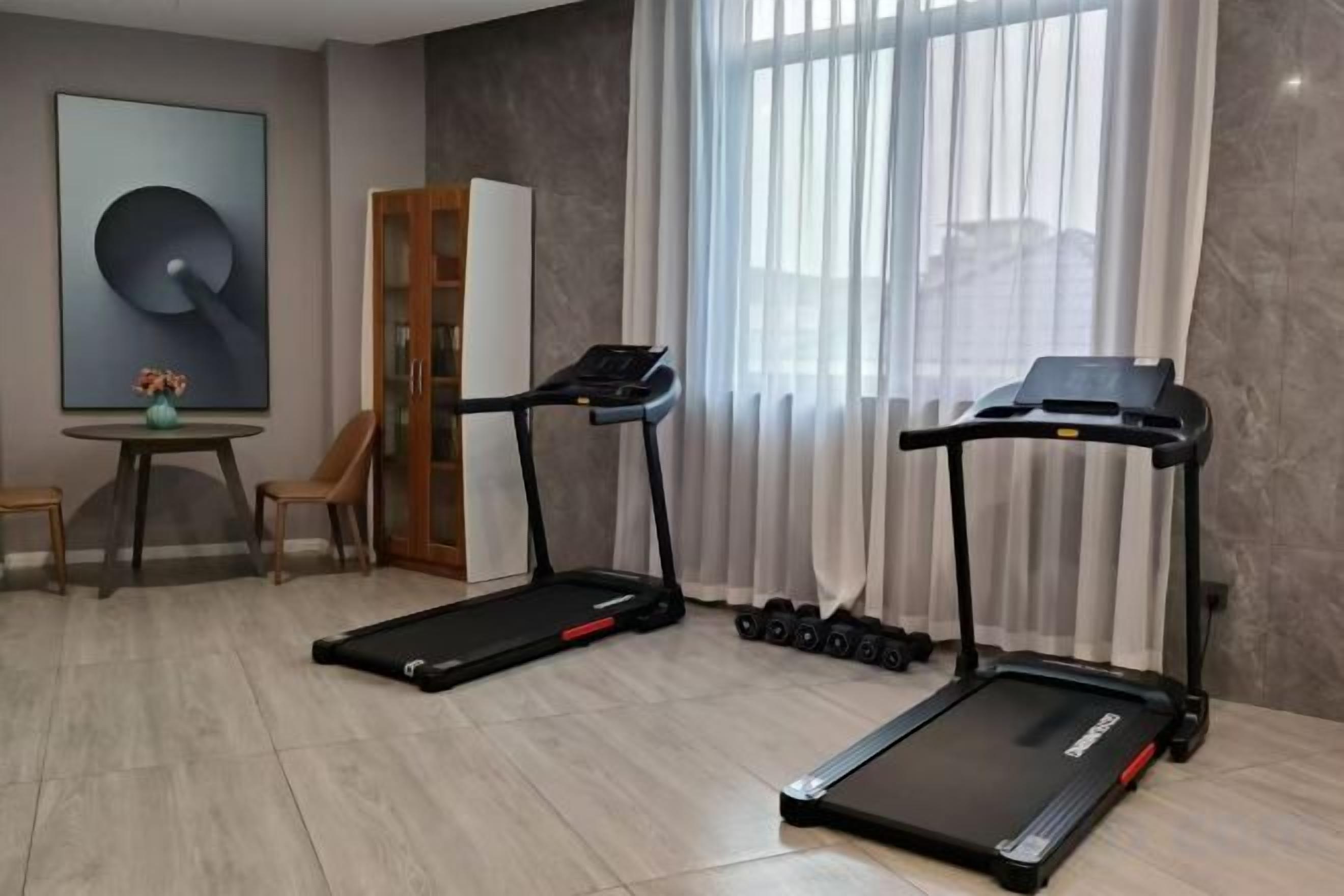 A room with two treadmills, a dining table with chairs, and a large window with curtains.