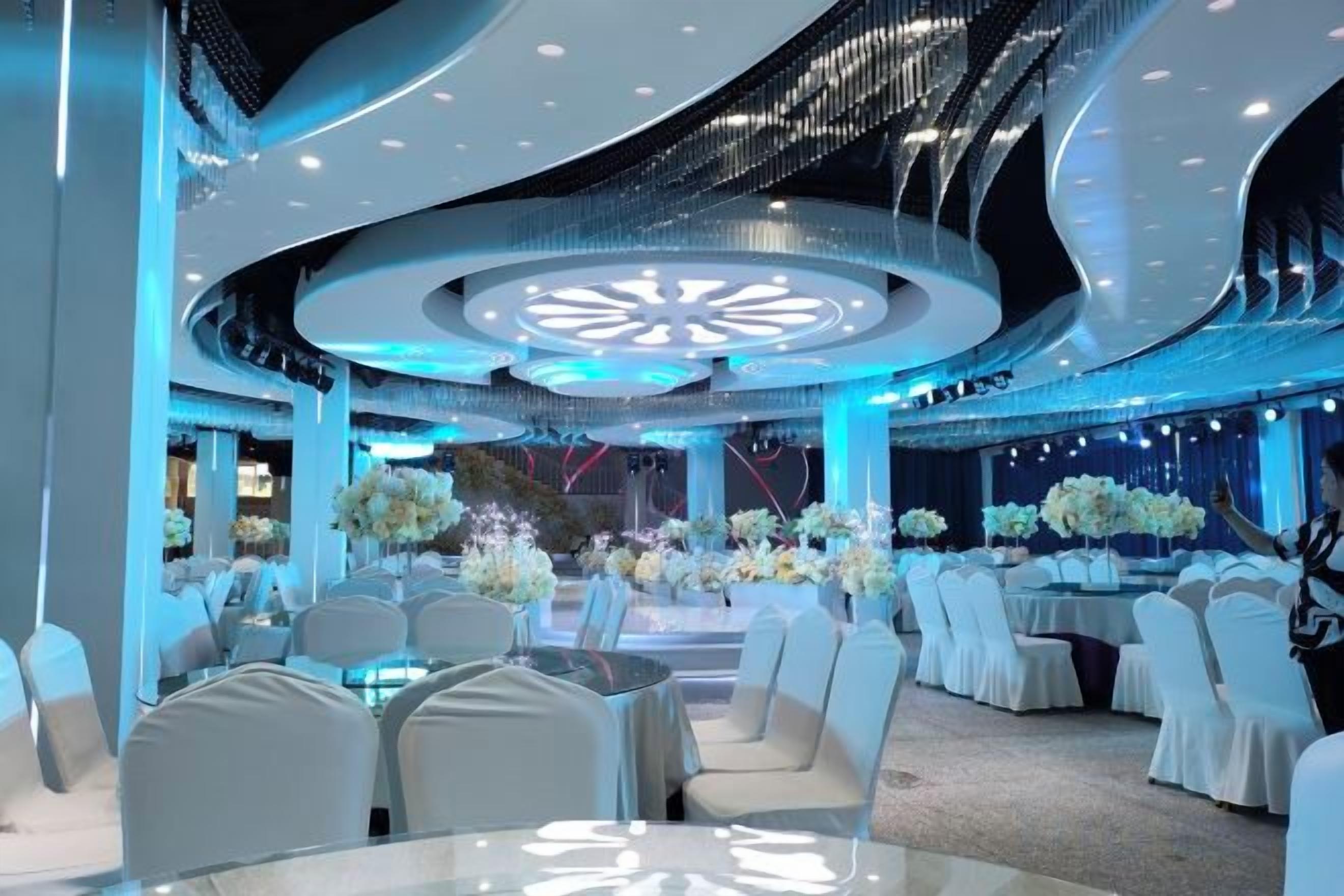 Una hall d'hotel moderna con tavoli rotondi, sedie bianche e composizioni floreali.