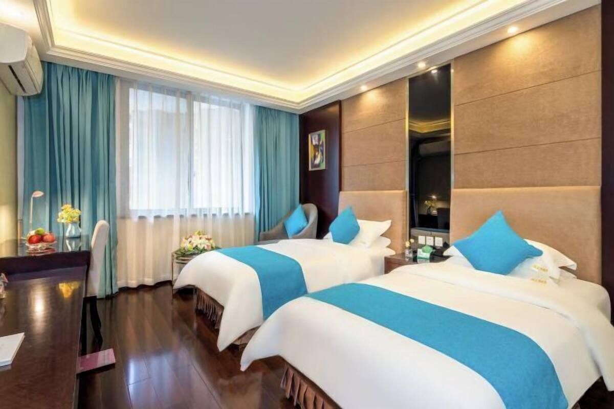 A hotel room with two beds, a desk, and a large window with curtains.