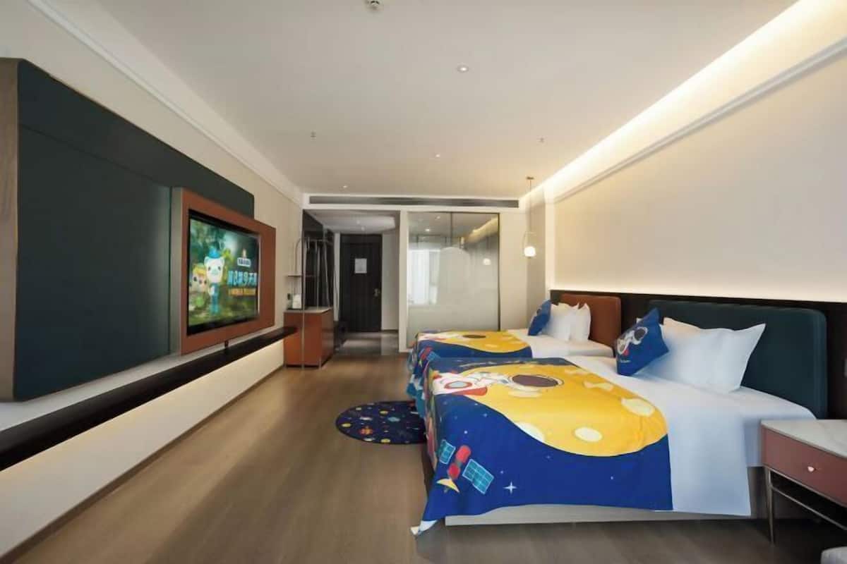 A hotel room with a large TV, two beds with space-themed bedding, a wooden floor, and a modern design.