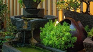 Un jardín japonés tradicional con una fuente de agua de piedra, un puente de madera y abundante vegetación.