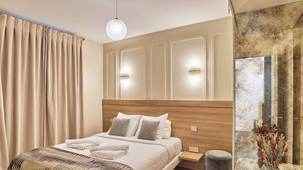 A modern bedroom with a wooden headboard, a large bed with white linens, a bedside table, a small stool, and a decorative vase. - Superb Air-conditioned Flat on the Champs Elysees (Paris)