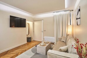 Ein modernes Wohnzimmer mit Flachbildfernseher, einer Couch, einem Couchtisch und einem Essbereich mit Tisch und Stühlen.