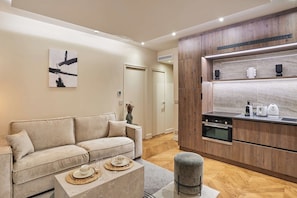 Una sala moderna con sofá, una mesa de centro y una cocina con armarios de madera y electrodomésticos.