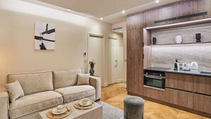 A modern living room with a sofa, coffee table, and a kitchen area with wooden cabinets and appliances. - Superb Air-conditioned Flat on the Champs Elysees (Paris)