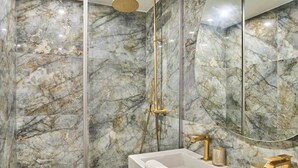 A bathroom with a marble wall, a glass-enclosed shower, a white sink, and gold fixtures. - Superb Air-conditioned Flat on the Champs Elysees (Paris)