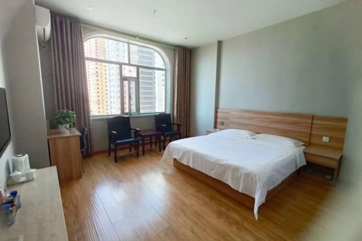 A hotel room with a bed, a desk, a chair, a window, and a plant.