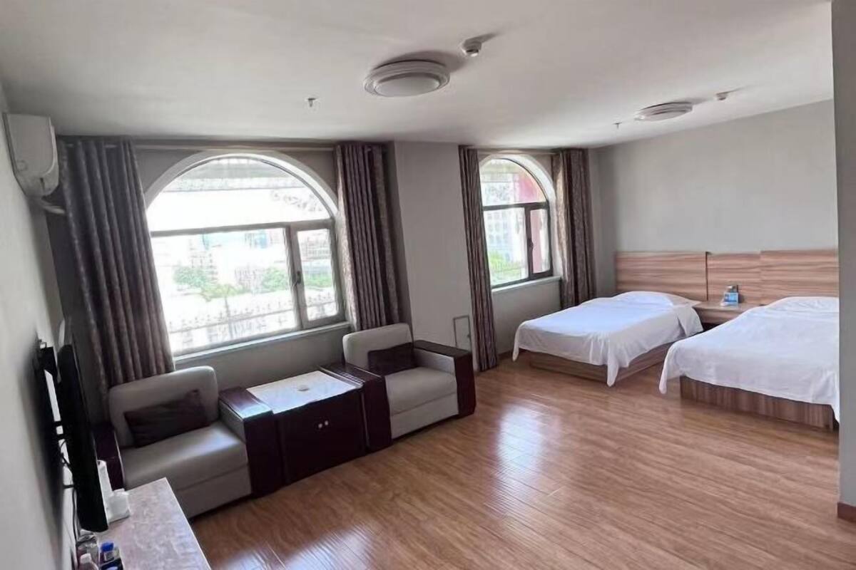 A hotel room with two beds, a sofa, a small table, and large windows with curtains.