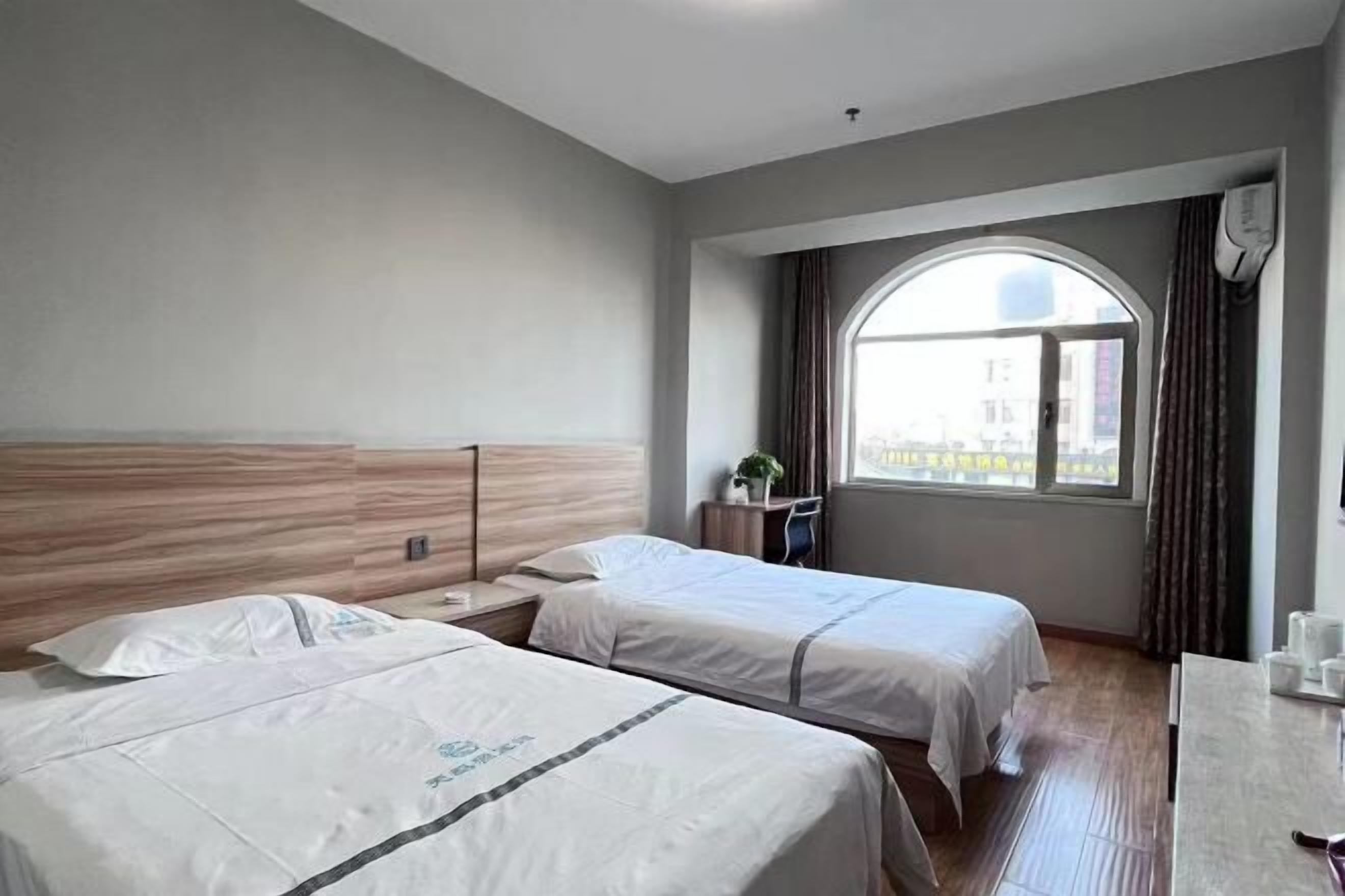 A hotel room with two beds, a large window, a desk, and a view of the city.