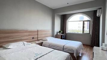 A hotel room with two beds, a large window, a desk, and a view of the city.