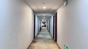 Un pasillo largo y estrecho con alfombra estampada, paredes blancas y puertas a ambos lados.
