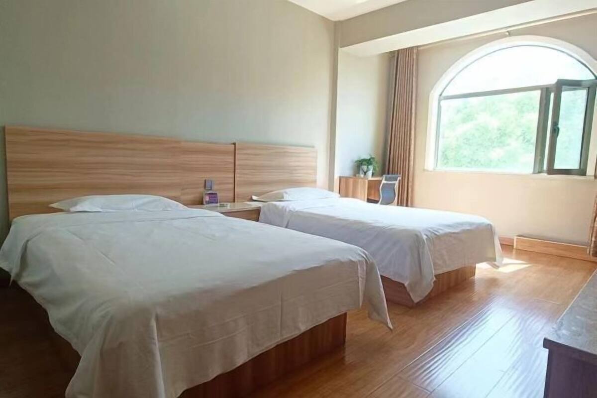 A hotel room with two beds, a wooden headboard, a nightstand, a desk, a chair, and a window with curtains.