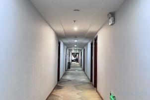 Un largo pasillo de hotel estrecho con puertas a ambos lados, alfombra estampada e iluminación empotrada en el techo.