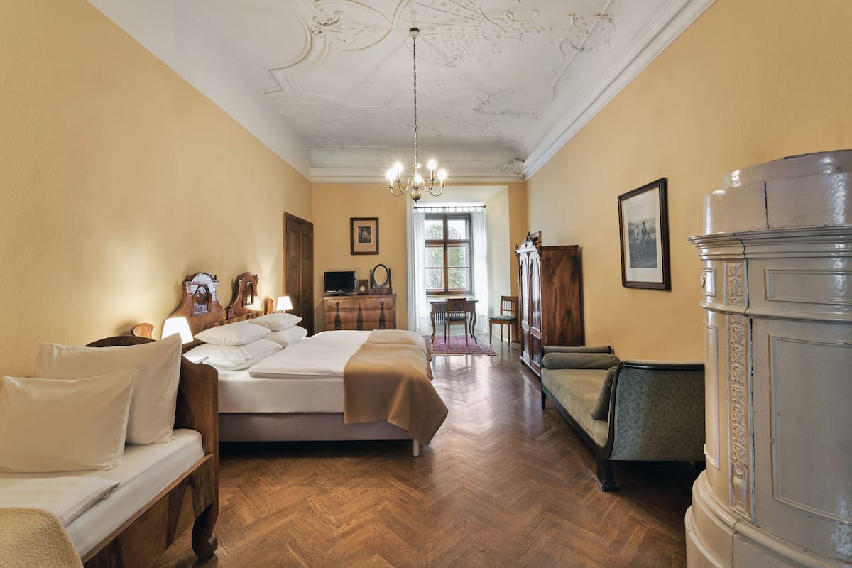 A hotel room with a bed, a desk, a chair, a wardrobe, and a chandelier.