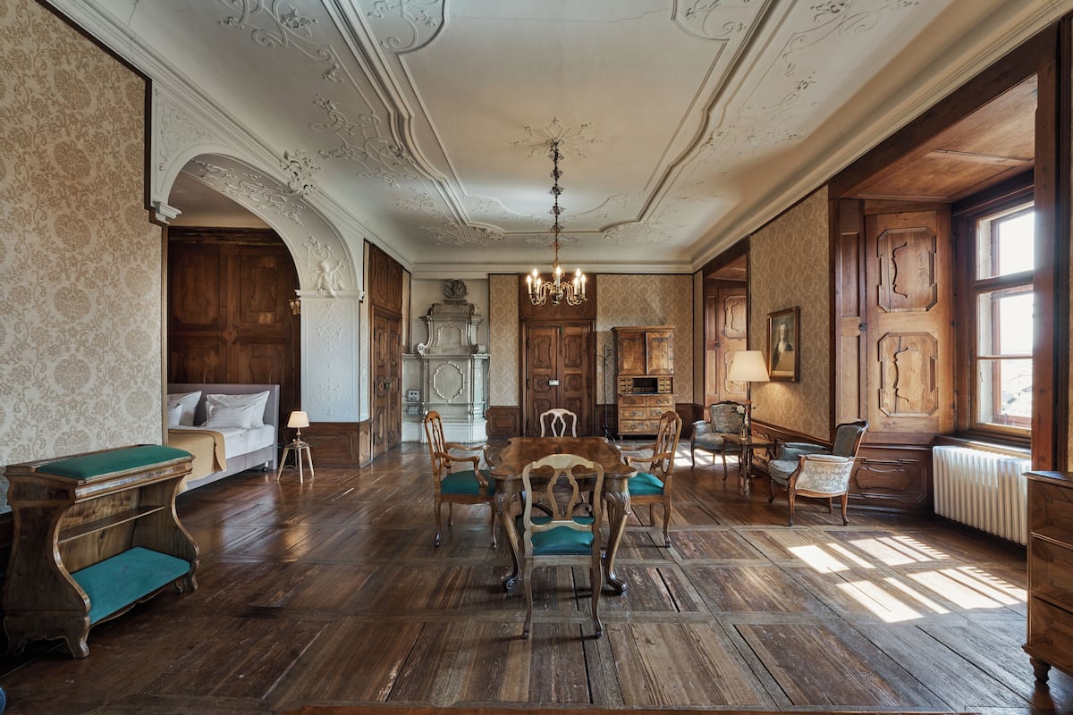 A room with a wooden floor, a dining table with chairs, a sofa, a fireplace, and a window.