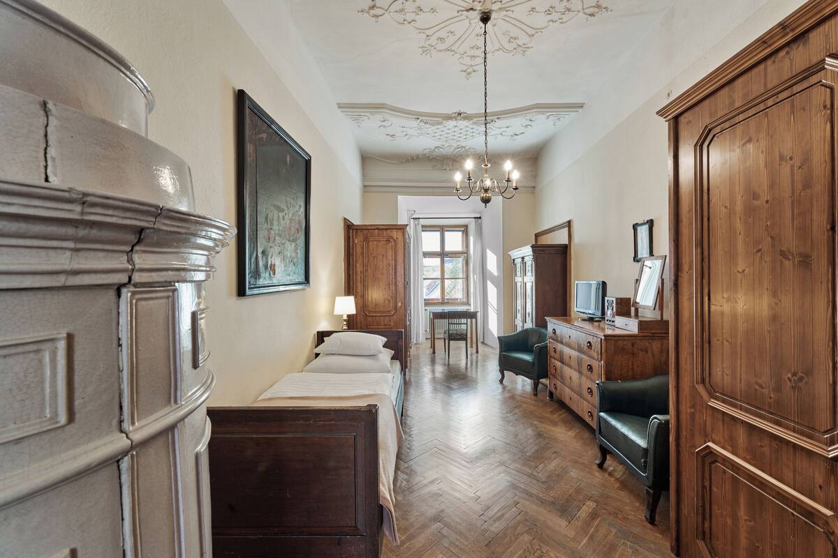 A room with a bed, wooden wardrobe, dresser, and a chandelier.