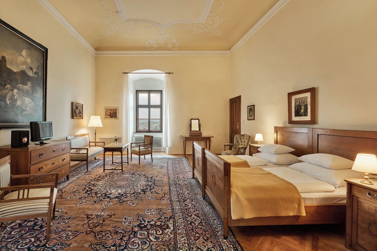 A hotel room with a large bed, a desk with a chair, a dresser, a television, and a large painting on the wall.