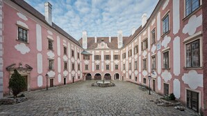 Un patio con pavimento de adoquines, una fuente en el centro y edificios rosados con detalles blancos y numerosas ventanas.