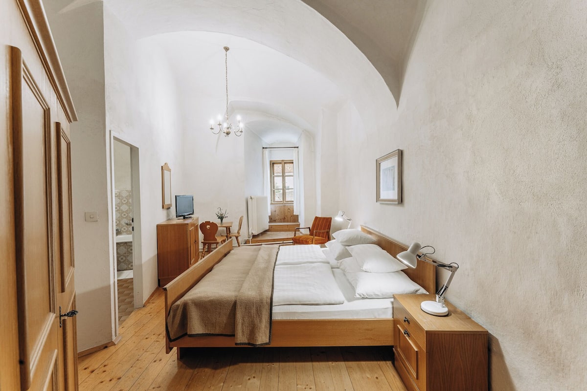 A bedroom with a wooden bed, a desk, a chair, a lamp, and a television.