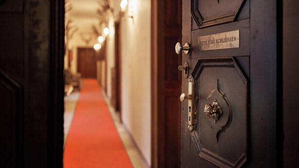 Entrada de un hotel con una alfombra roja que conduce a una puerta de madera con un letrero que dice "Bitte Tür Schließen".