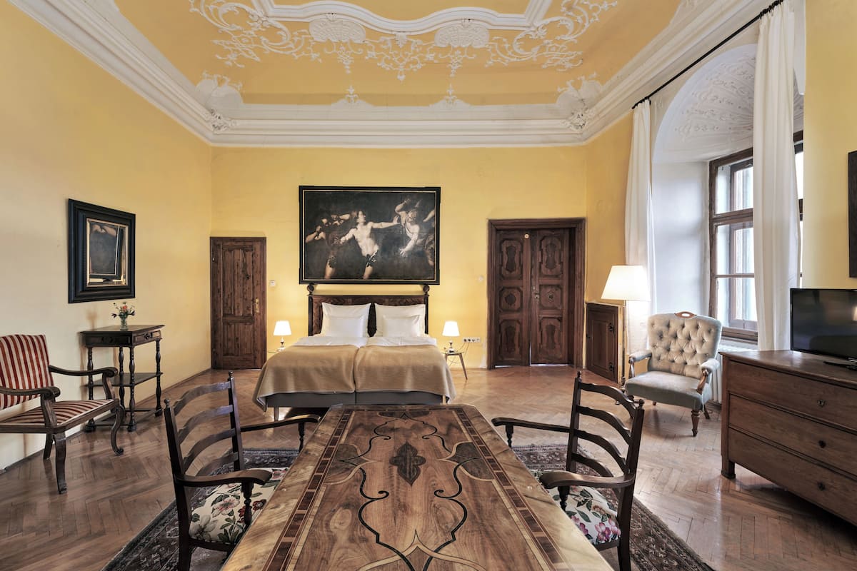 A hotel room with a large bed, a television, a dining table, and a painting on the wall.